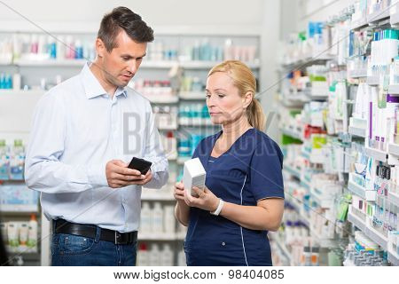 Mid adult male customer showing product information on mobile phone to pharmacist in pharmacy