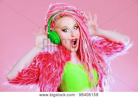 Trendy DJ party girl in bright clothes, headphones and with bright pink dreadlocks. Disco, party. Show business. Bright fashion.