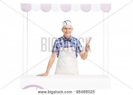 Studio shot of an ice cream vendor holding an ice cream cone and posing behind a stall isolated on white background