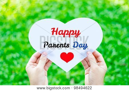 Hand Holding White Heart Paper With Happy Parents Day Text On Blur Green Grass Background