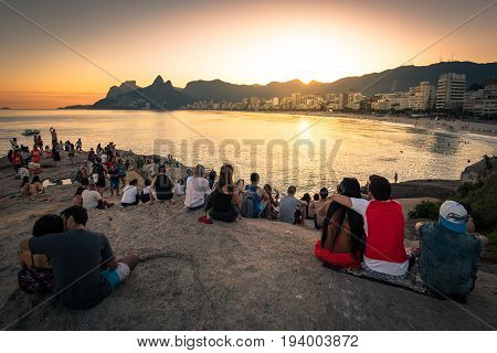 Rio de Janeiro, Brazil - June 30, 2017: People sitting all around on Arpoador rock and enjoying beautiful sunset.
