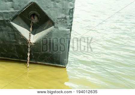 Prow of old rusty dark ship with anchor chain anchored in green Danube river. Novi Sad, Serbia.