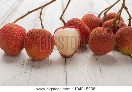 fresh lichees with one piece half peeled on white wood background