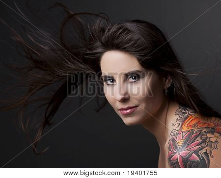 Ritratto di una donna bella e con un tatto sulla spalla contro uno sfondo grigio e capelli di diffusione