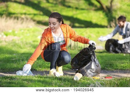 Young beautiful volunteer picking up litter in park