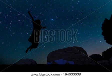 Silhouette of young woman jumping over sand hill beneath the stars Milky Way and a lot of stars over the mountain at Wadi Rum desert. Concept for happiness traveling and freedom.