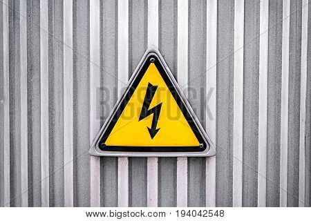 High voltage yellow triangle warning sign on gray metal wall. Danger electricity warning sign. Black lightning arrow symbol on yellow background in triangle