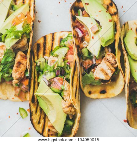 Healthy corn tortillas with grilled chicken fillet, avocado, fresh salsa, limes over light grey marble table background, top view, square crop. Gluten-free, allergy-friendly, weight loss concept