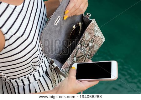 Fashionable woman holding luxury snakeskin python bag. Elegant outfit. Close up of purse in hands of stylish lady. Model posing near the swimming pool.
