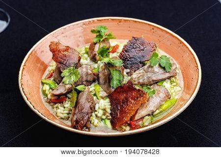Baked duck served in a plate with rice and green beans and greens dressed with sauce.
