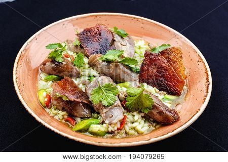 Baked duck served in a plate with rice and green beans and greens dressed with sauce.