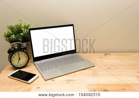 Laptop computer with white blank screen mobile smart phone and black vintage retro alarm clock times at 7 o'clock morning on wooden table workspace selective focus copy space vintage color tone
