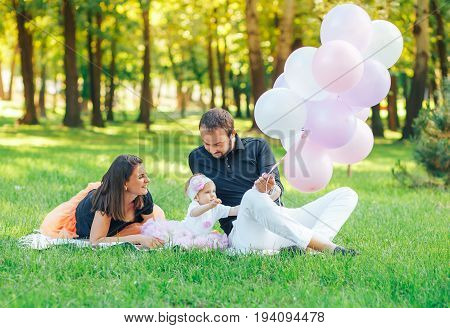 happy family resting in the Park on the grass. Father holding a lot of balloons in hand