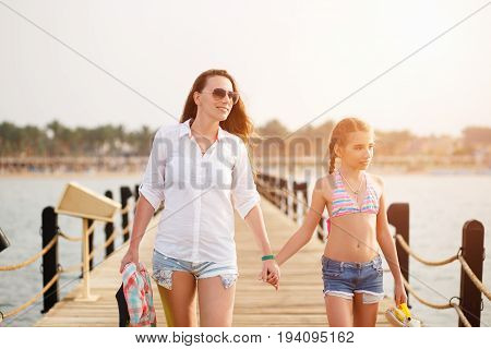 Young woman with her daughter strolling along pier on sea vacation
