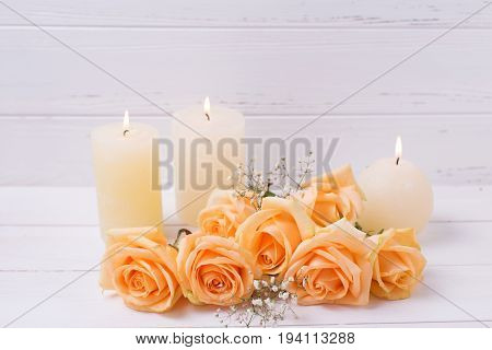 Candles and peach color roses flowers on white wooden background. Shubby chic. Place for text. Selective focus.