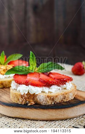 A small bruschetta with curd and fresh strawberries on a dark wooden background. Proper nutrition. Vertical view.