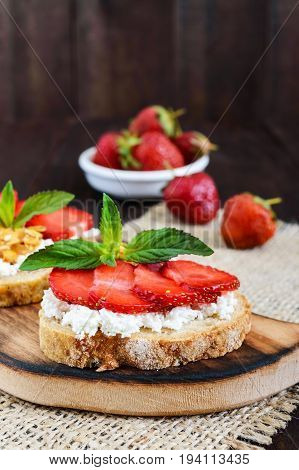 A small bruschetta with curd and fresh strawberries on a dark wooden background. Proper nutrition. Vertical view.