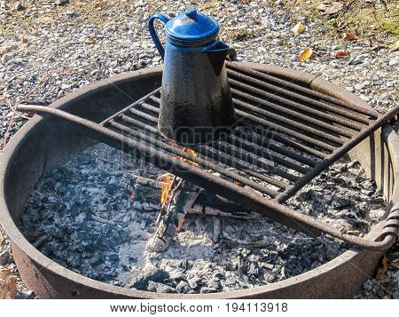 Blue tea water kettle on grill in fire pit at campground