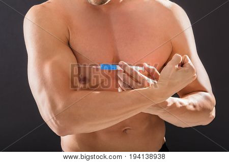 Shirtless Bodybuilder Man Using Steroids By Injecting Syringe In His Arm Against Black Background