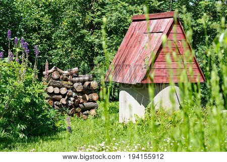 Rustic Wooden Water Well With Woodpile Of Firewood