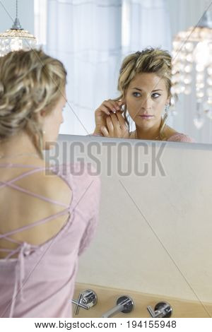 A woman in front of the mirror wearing earrings
