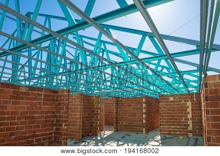New residential brick house construction with roof metal framing against a blue sunny sky. Construction site inner view