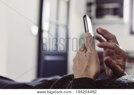 closeup of a young caucasian man using his smartphone lying down on a couch or a bed