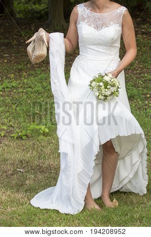 Bride barefoot with shoes in the hand and green and white bouquet in the other hand