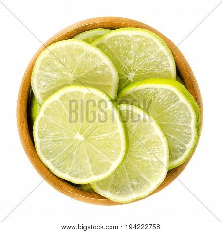 Lime slices in wooden bowl. Fresh cut unripe green edible citrus fruit discs. Key lime, Citrus aurantiifolia. Isolated macro food photo close up from above on white background.