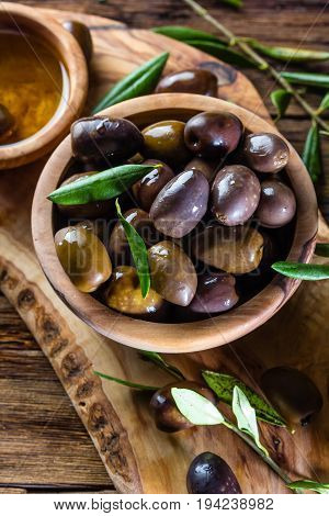 Olives and olive oil in olive wooden bowls on olive wooden cutting board, olive tree branch on wooden rustic background