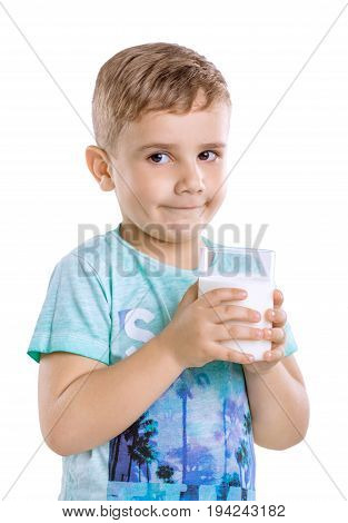 A cute little blonde baby boy in blue t-shirt is holding a glass of organic milk isolated on a white background close-up.