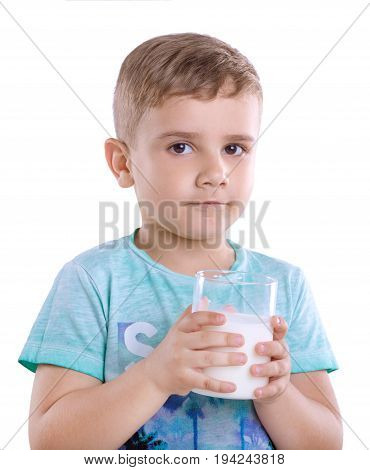 Curious little kid wearing blue t-shirt with a glass full of nutritious milk isolated on a white background. Tiny cute boy wearing in a blue t-shirt is holding a full glass of milk isolated on a white background.