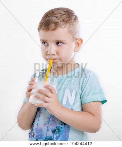 Cute little boy holding a glass of milk and drinking fresh milk. A little kid standing in blue shirt and drinking milk in a glass from a yellow straw. A nice little kid with milk. Healthcare.