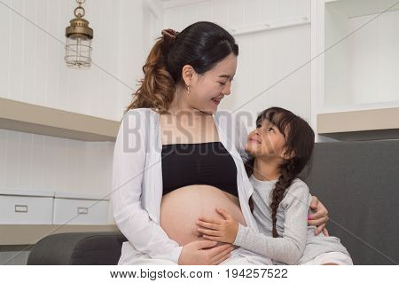 The girl is listening to belly of pregnant mother