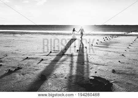 Happy man and woman couple walking and holding hands on a beach with bright colorful sunrise on the background, romantic couple in love walking at sunset, woman and man in love walking hand in hand