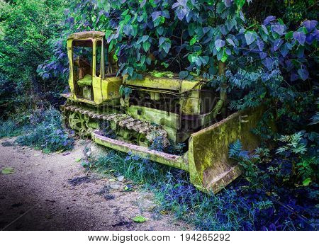 Old fashion antique worn rusted construction full track crawler yellow tractor among green trees. Hue construction industry machine crawler tractor blade vehicle. Abstract tractor background texture