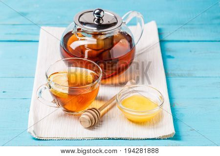 Glass cup of tea with lemon, glass teapot and honey on blue wooden table.
