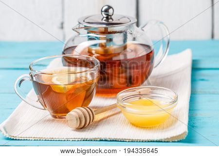 Glass cup of tea with lemon, glass teapot and honey on blue wooden table.