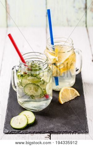 Two mugs of infused detox diet refreshing waters: with cucumber and lemon on white wooden table