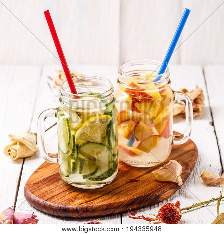 Two mugs of infused detox diet refreshing waters - first with cucumber and lemon, second with lemon and peach on white wooden table