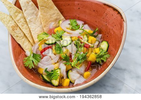 Fresh Mango Salsa with raw fish filet in brown plate on marbel desk