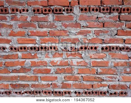 Red brick wall with grey mold. Three horizontal lines of black round holes. Taken in daylight.