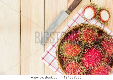fresh tropical rambutan fruits over basket with knife on wood background Top view with copy space and text.