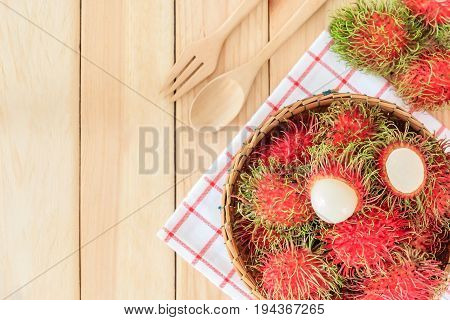 fresh tropical rambutan fruits over basket with spoon and fork on wood background Top view with copy space and text.