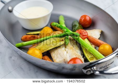 Grilled fish and vegetables with sauce served in metalic bowl on marble serface