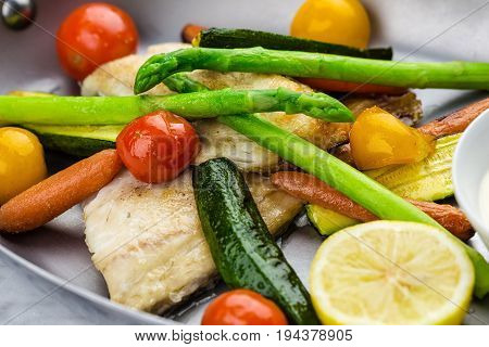 Grilled fish and vegetables with sauce served in metalic bowl on marble serface