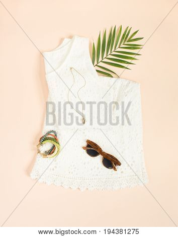 Summer fashion summer outfit on cream background. White lace dress retro sunglasses wood bracelet. Flat lay top view