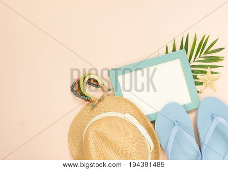 Empty frame and summer holidays items on creme background. Straw hat blue flip flops and wood bracelet. Selective focus. Place for text. Flat lay top view.