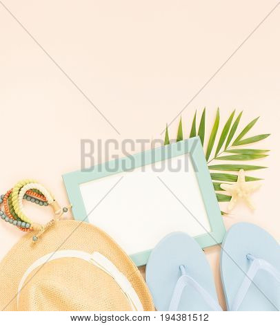 Empty frame and summer holidays items on creme background. Straw hat blue flip flops and wood bracelet. Selective focus. Place for text. Flat lay top view.