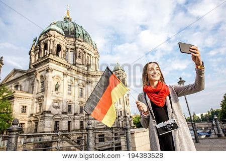 Young woman tourist making selfie with german flag in front of the famous cathedral in Berlin city